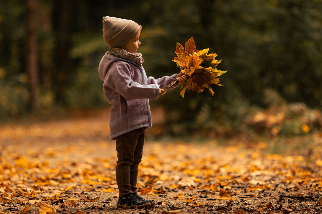 Kind steht mit bunten Blättern im Herbstwald.