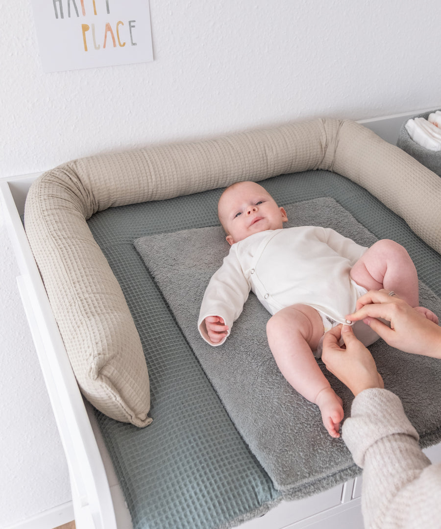 Vielseitig einsetzbar*Auf dem Wickeltisch sorgt die Bettschlange für Sicherheit und Komfort beim Wickeln.|Baby liegt auf dem Wickeltisch, am Rand rundherum liegt die Bettschlange in beige.