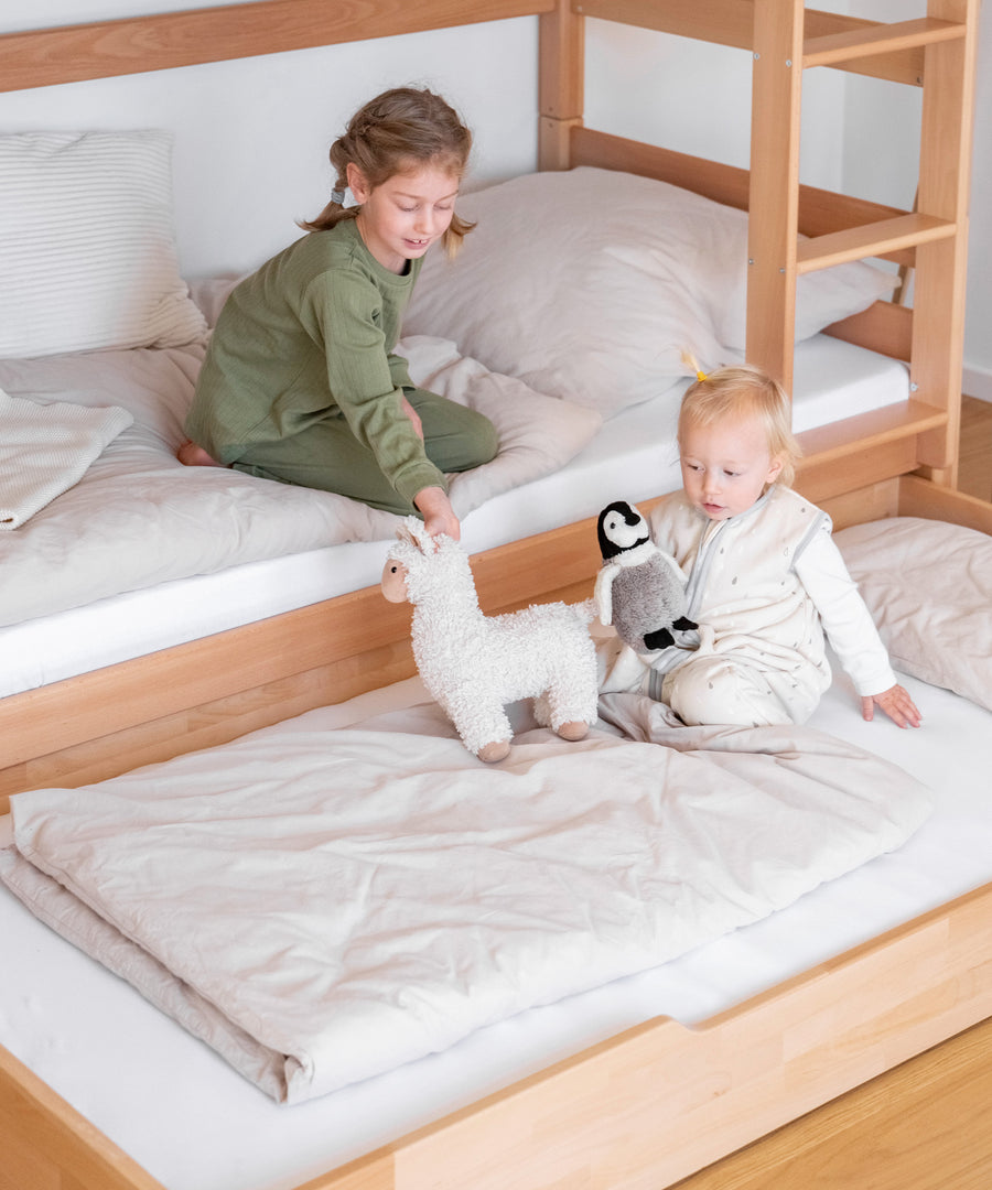 Zusätzlicher Schlafplatz*Für Übernachtungsgäste oder Eltern: Mit dem optionalen Bettkasten kann man ganz einfach einen weiteren Schlafplatz zaubern.|Mädchen sitzt im unteren Bett des Etagenbetts, auf dem ausgezogenen Bettkasten davor sitzt ein Geschwisterkind.