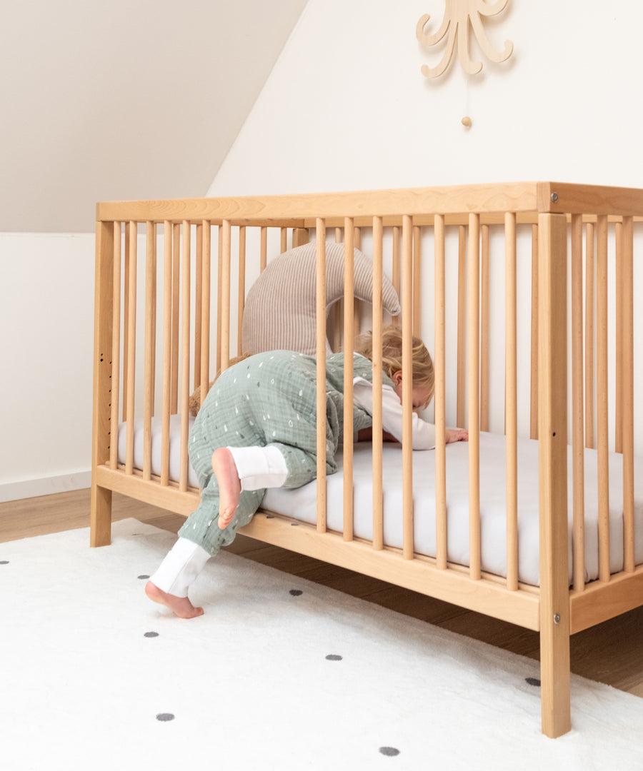 Fördert die Selbstständigkeit*Durch die herausnehmbaren Stangen kann dein Kind ganz alleine ein- und aussteigen. Der Rausfallschutz bleibt dabei erhalten.|Mädchen krabbelt in Babybett Natur.