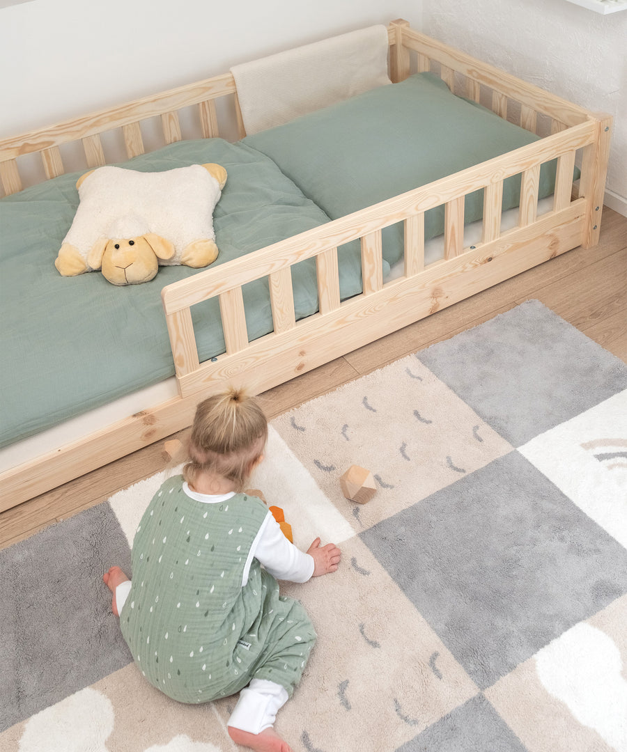 Mädchen spielt auf Teppich vor bodentiefem Kinderbett aus Kiefer.