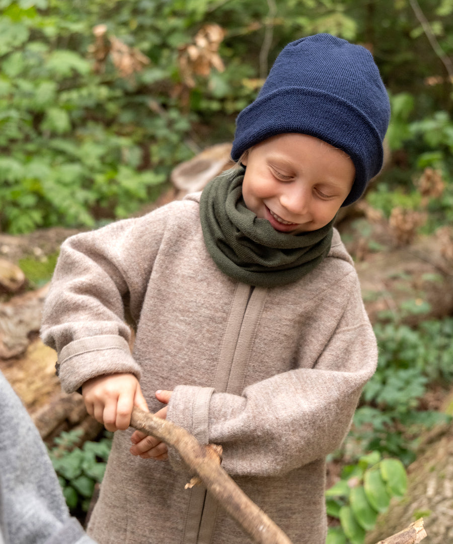Made in Germany*Die hochwertige Strickmütze im zeitlosen Design wird in Deutschland produziert.|Junge mit Strickmütze und Schlauchschal spielt im Wald.
