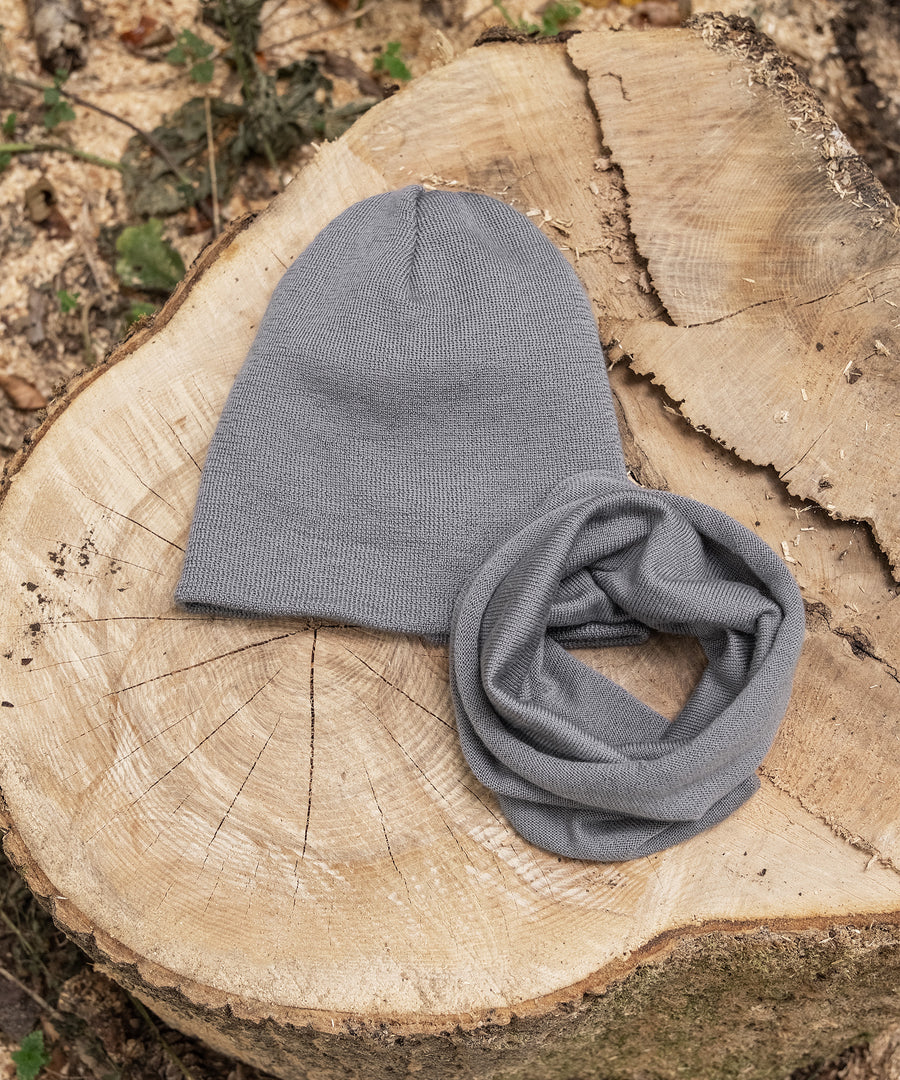 Passend erhältlich*Passend zur Strickmütze ist der Schlauchschal im Shop erhältlich.|Strickmütze und Schlauchschal in Grau liegen auf Baumstumpf.