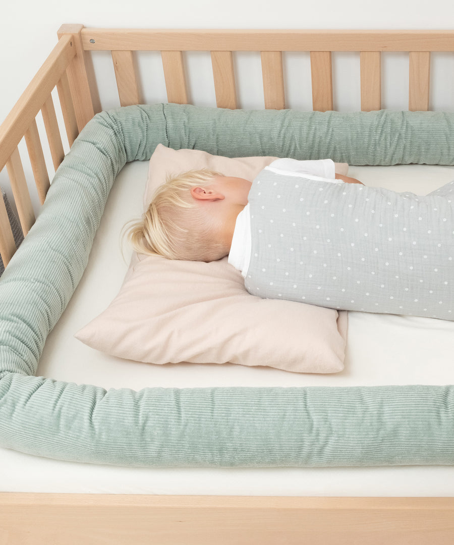 Waschbar & pflegeleicht*Die Bettschlange kann bei 30 °C in der Waschmaschine gewaschen werden – für hygienische Frische im Alltag.|Kind liegt im Kinderbett umrandet von einer Bettschlange in Jade.
