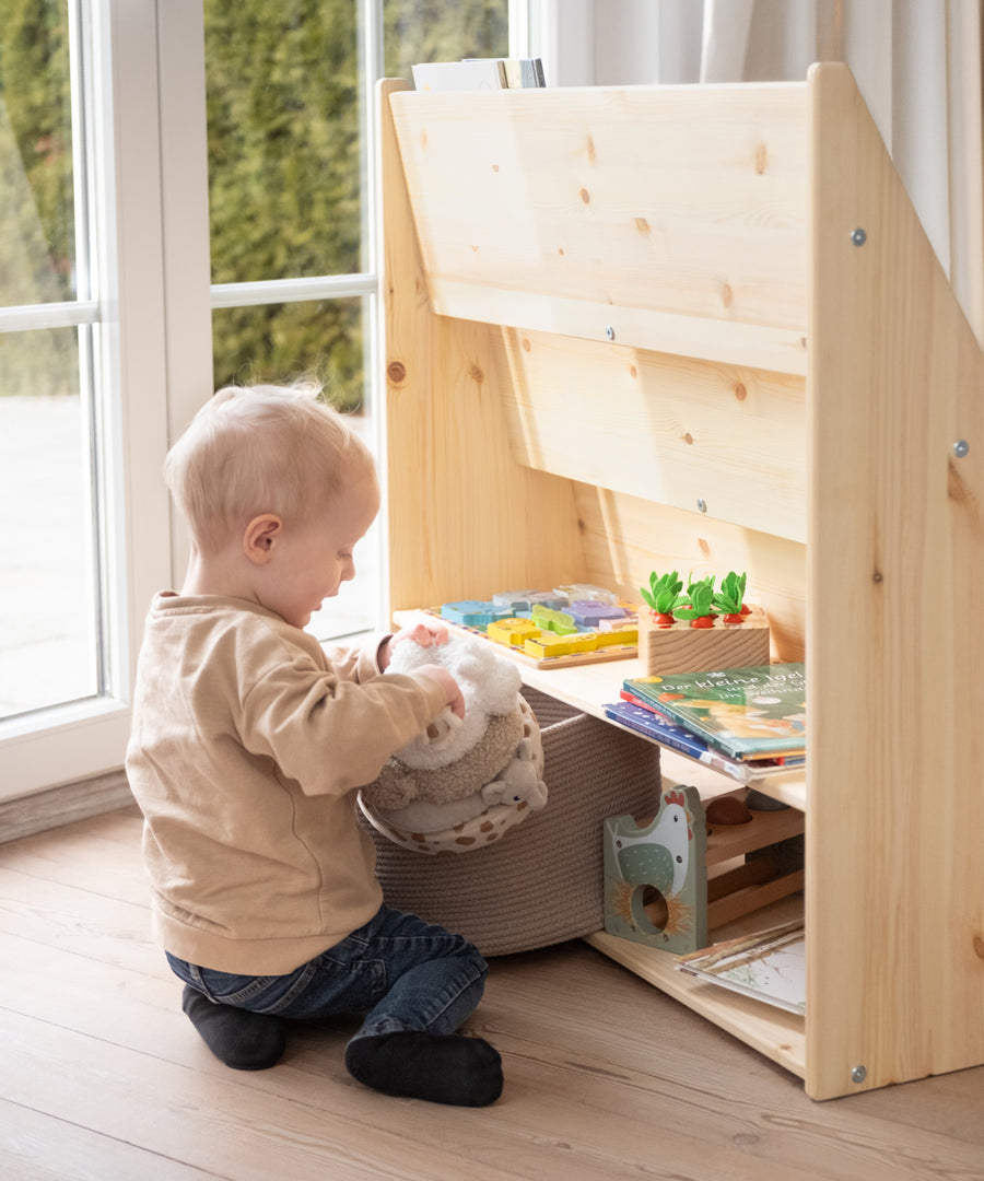 Praktischer Extra-Stauraum*Auf der Rückseite lassen sich Bücher und Spielzeug verstauen, die gerade nicht genutzt werden - ideal zum Rotieren.| Kind nimmt selbstständig Bücher und Spielzeug aus dem Stauraum auf der Rückseite des Regals.