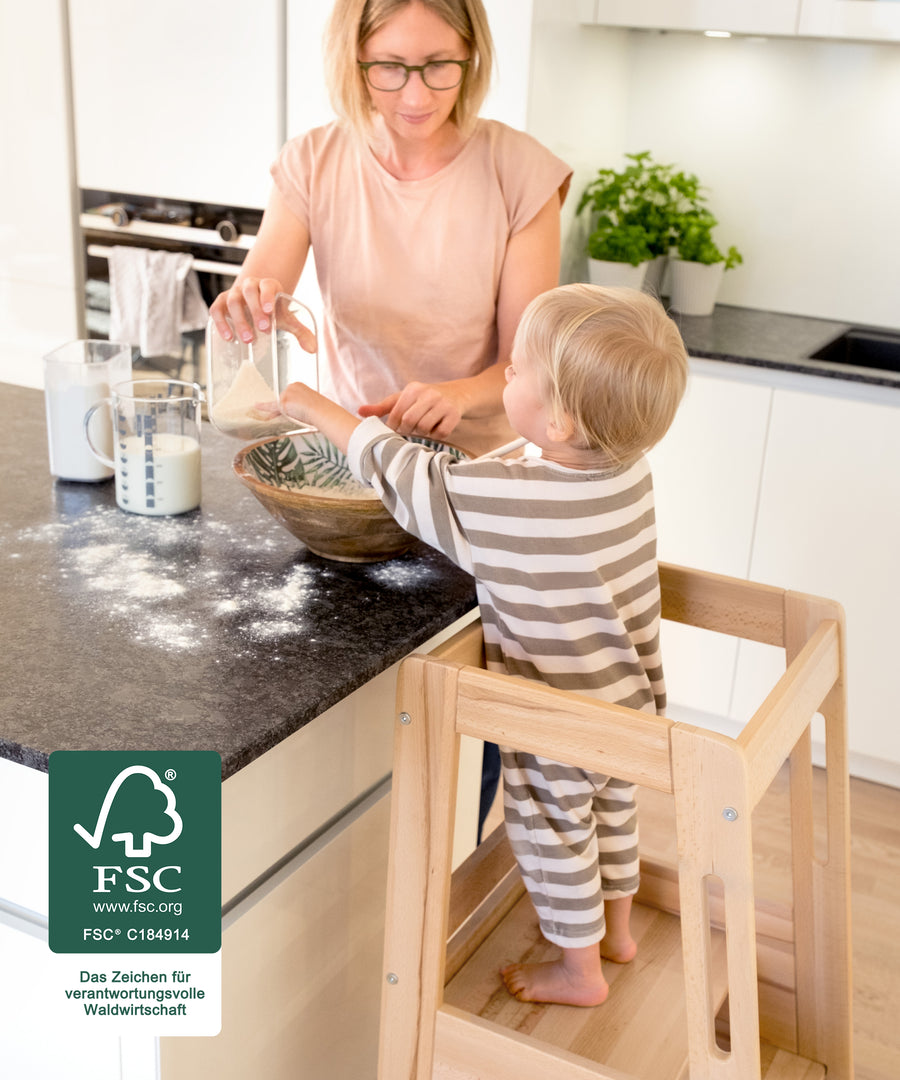 Kind steht im Lernturm und hilft beim Backen in der Küche.