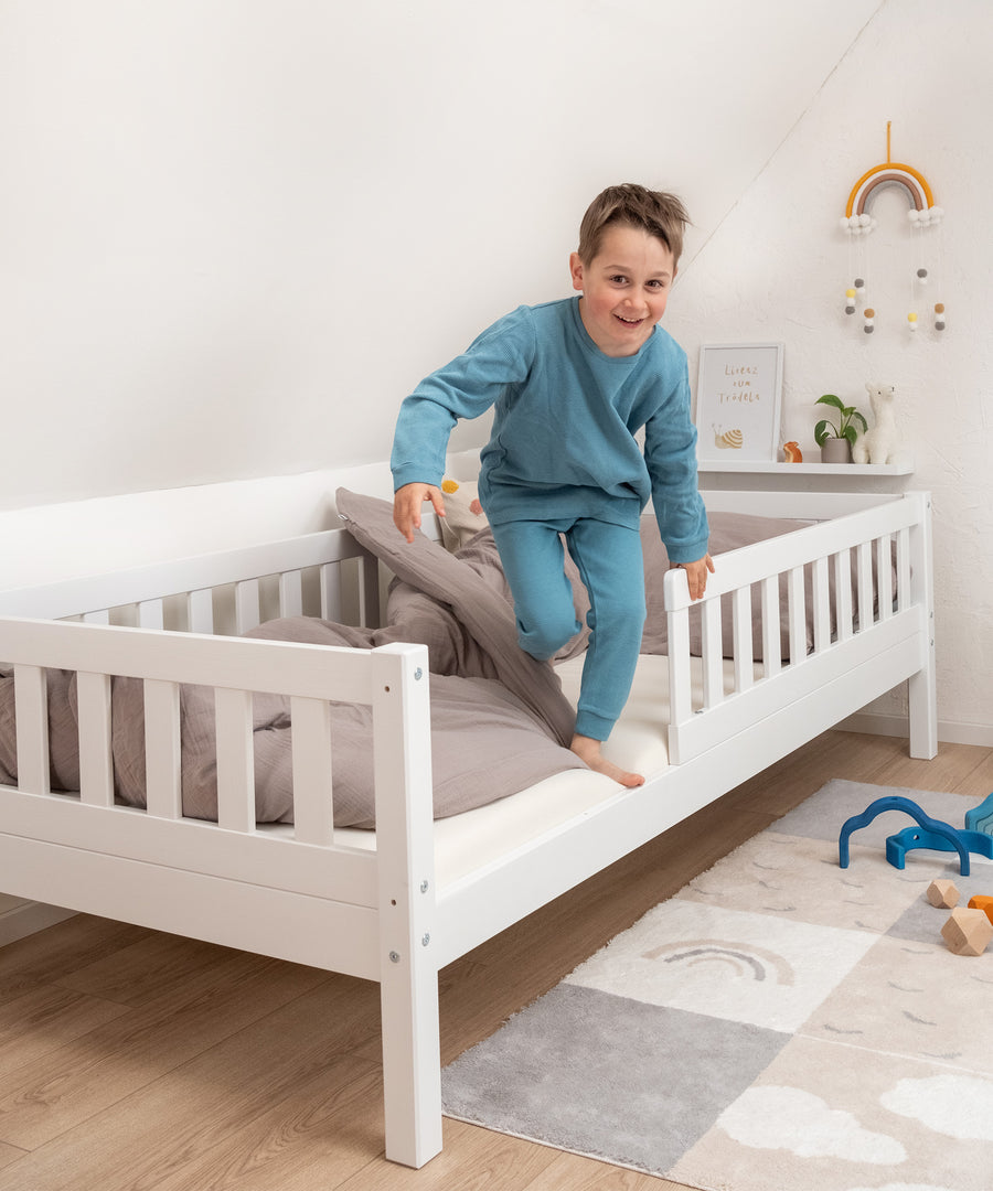 Junge steigt lachend aus Kinderbett Kiefer weiß.