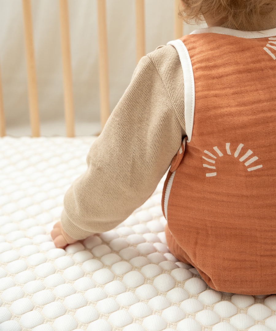 Baby auf kühlender Matratzenauflage in Gitterbett.