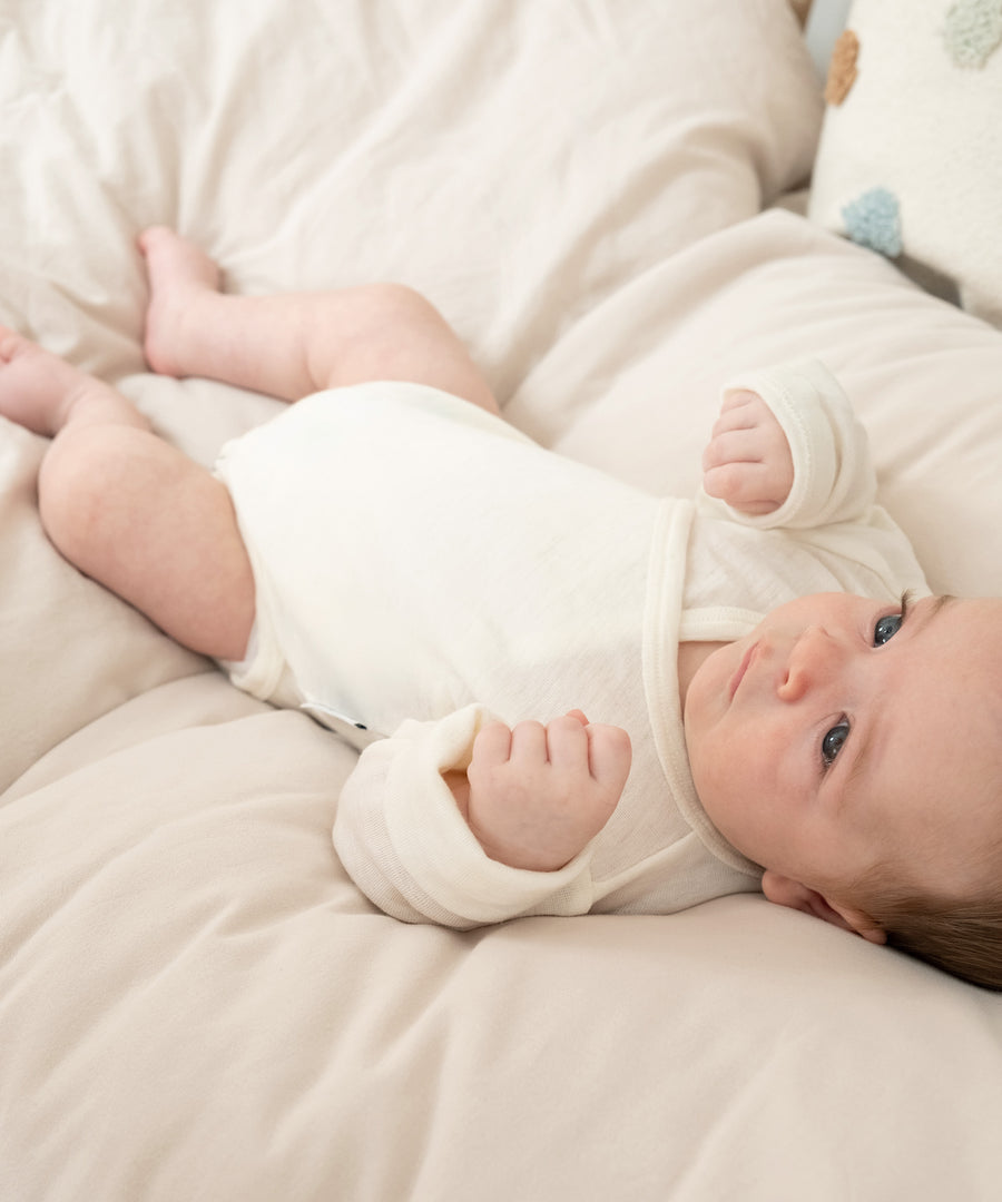 Baby in Wickelbody liegt auf Bett.