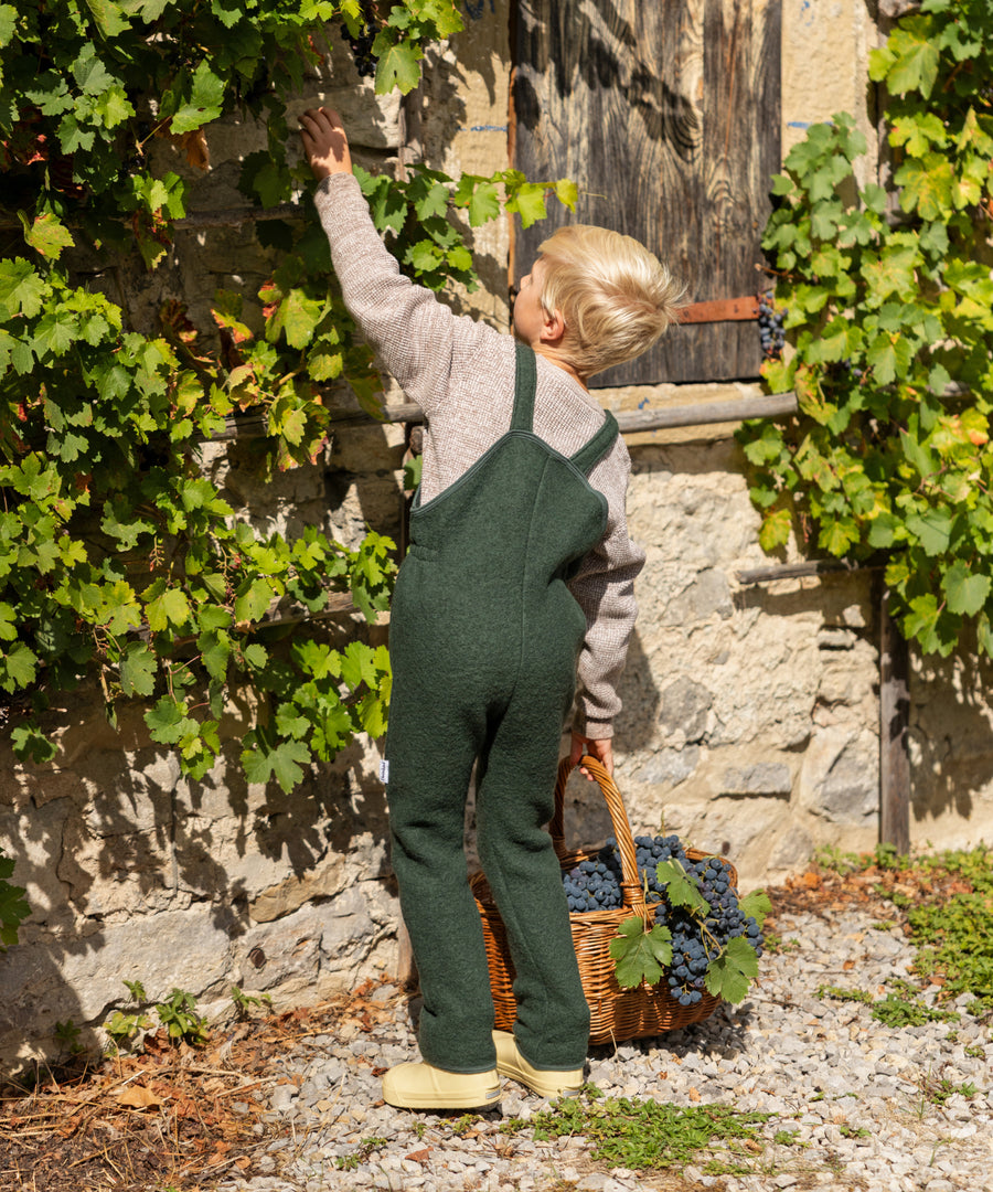 Flauschiger Wollwalk*Das hochwertige Material aus 80 % Bio-Schurwolle und 20 % Bio-Baumwolle ist kuschelweich und atmungsaktiv.|Kind trägt die Walk-Latzhose in Waldgrün.